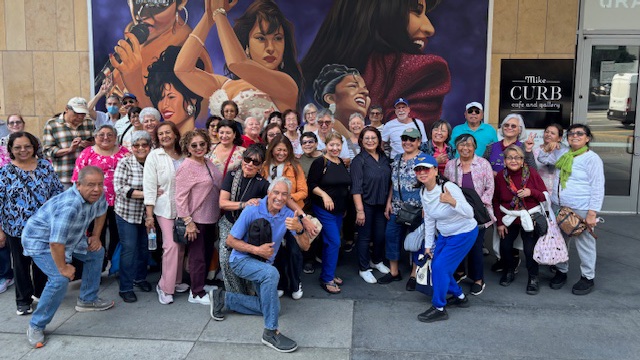 A large group from the Glassell Park center poses together on the sidewalk in front of a big framed artwork outside the Grammy Museum, with two men crouching in the front row.