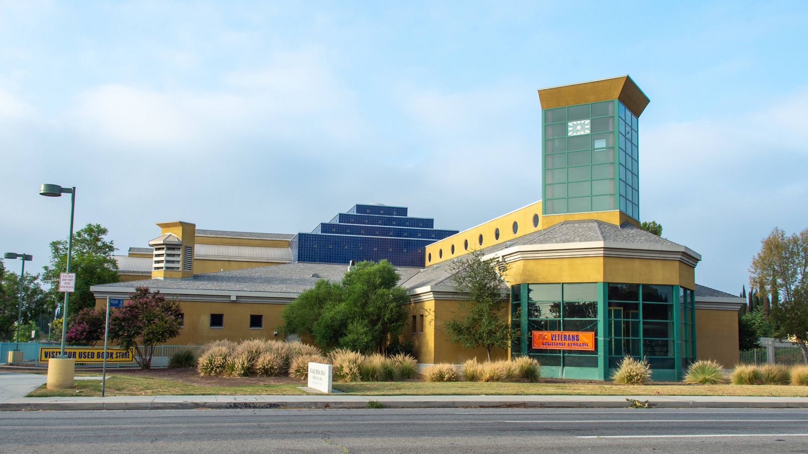 Street view of the Mid-Valley Regional Branch Library in North Hills, a gold stucco building with a green glass clock tower and a blue stepped roof, where the class meets